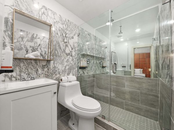 A modern bathroom with a marble-pattern wall, glass shower enclosure, white vanity, and a toilet, all in a sleek, bright layout.