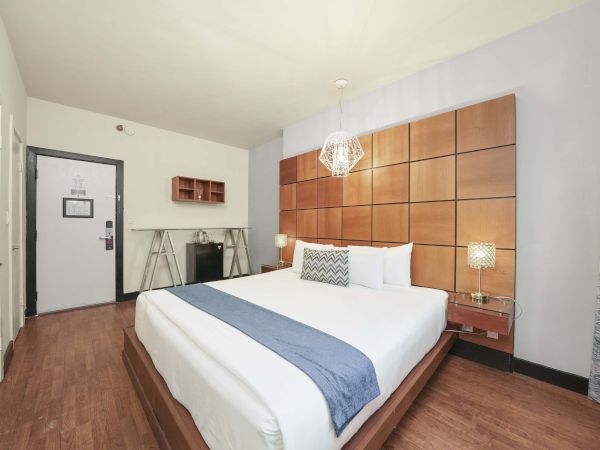 A modern hotel room with a large bed, wooden paneled accent wall, nightstands, a chandelier, and a small desk area near the door, cozy and stylish.