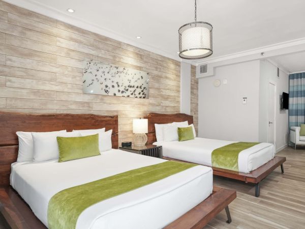 Two double beds in a modern hotel room with a wood headboard, lime‑green accents, a small nightstand, and a mix of white and blue decor, ending with a vibe of calm luxury.