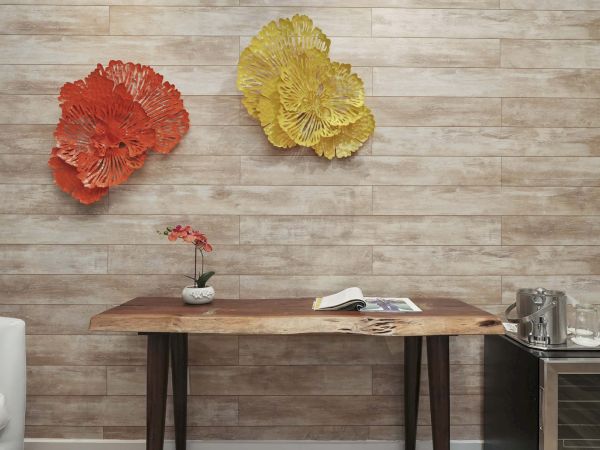 A modern room with a wooden desk, a small potted flower, scattered papers, and two large yellow and red textured wall art pieces hanging above it.