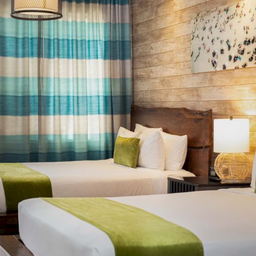 Two twin beds in a modern hotel room with a wooden feature wall, striped teal curtains, green accents, and a bedside lamp, cozy and stylish.