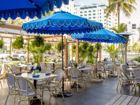 Outdoor cafe scene with blue striped umbrellas, wicker chairs, and tables set for dining along a sunny patio. End.